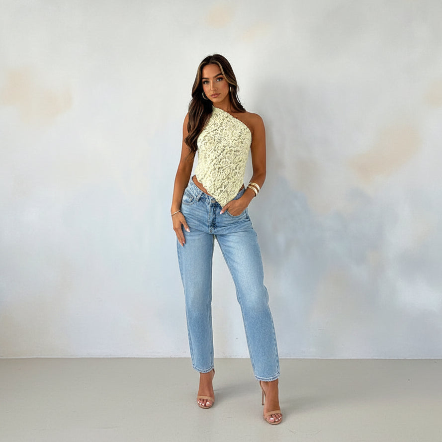Woman wearing a yellow lace top and blue jeans against a plain background