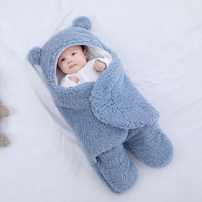 Baby wrapped in a blue fluffy bear-shaped swaddle on a white background