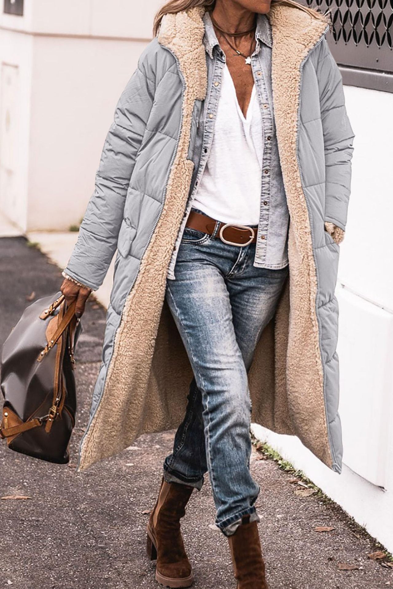 Person wearing a long gray puffer coat with a beige hood, white shirt, blue jeans, and brown boots.