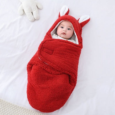 Baby wrapped in a red fox-themed swaddle on a white blanket