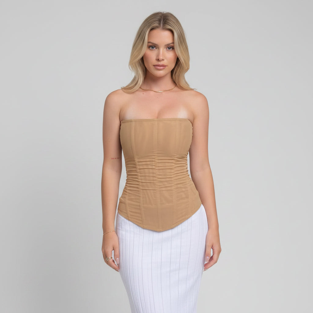 Woman wearing a beige strapless top and white pants standing against a black door.
