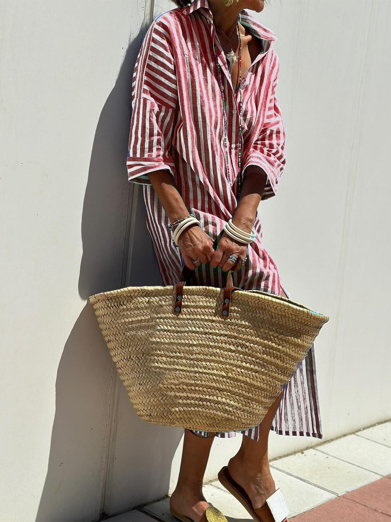 Person wearing a red and white striped shirt holding a straw bag against a white wall.