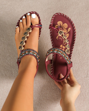 Maroon sandals with floral embroidery and colorful straps on a neutral background