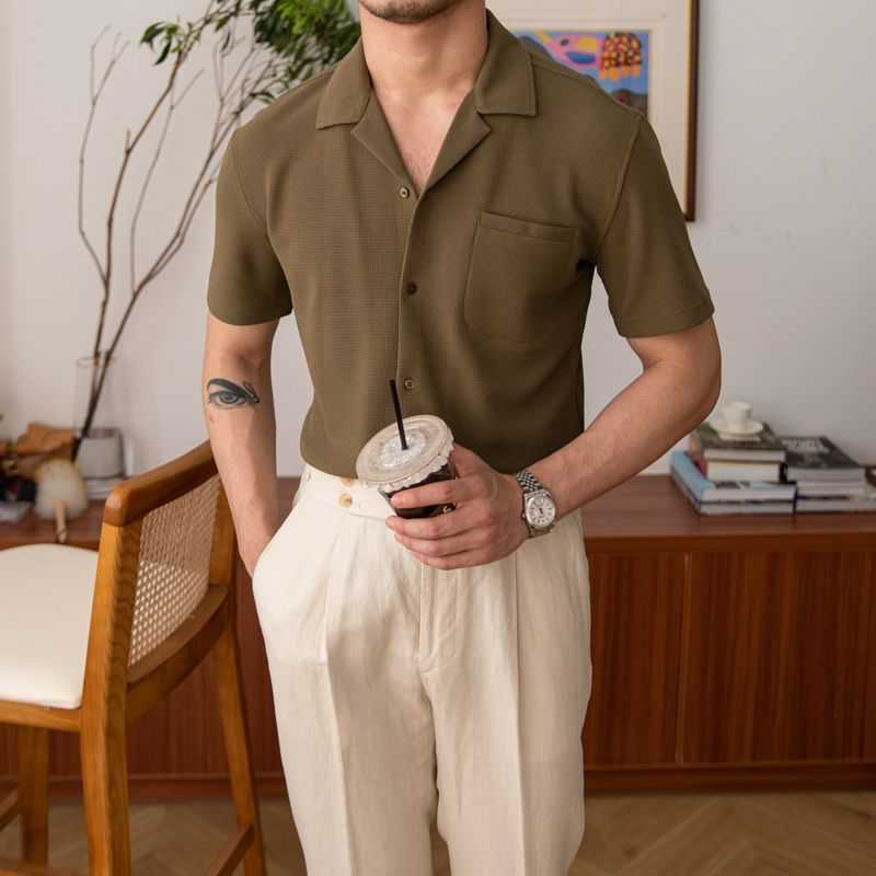 Man wearing a brown shirt and white pants holding a coffee cup indoors.
