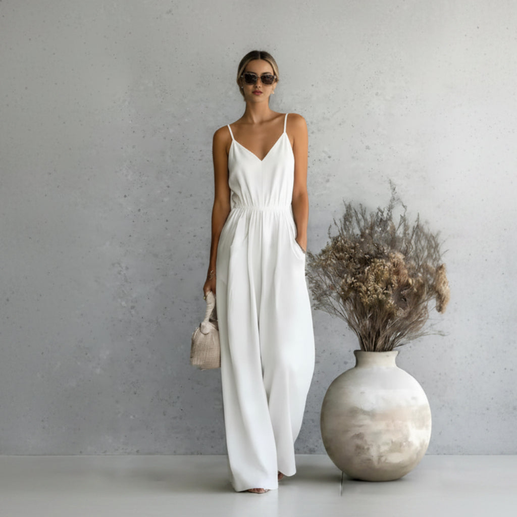Woman in a white dress standing next to a vase with dried flowers against a gray wall.