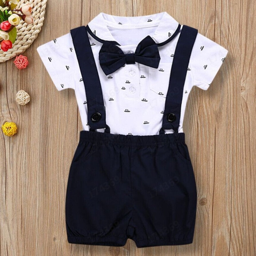 Baby outfit with white shirt, navy suspenders, and shorts on a wooden surface.