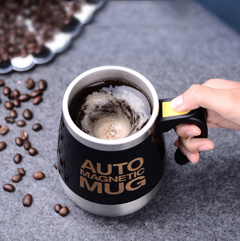Black mug with 'Auto Magnetic Mug' text, filled with coffee, held by a hand with coffee beans around.