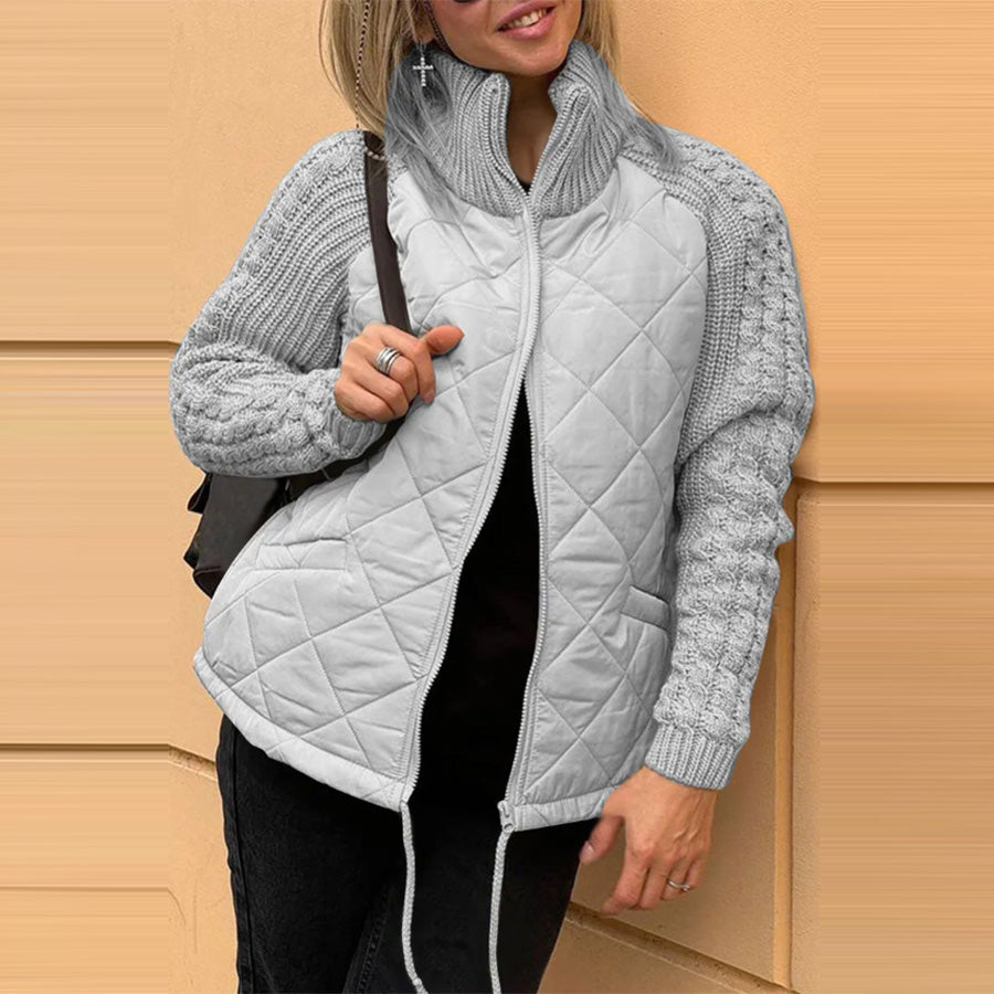 Person wearing a gray quilted jacket with a textured sleeve design against a beige wall.