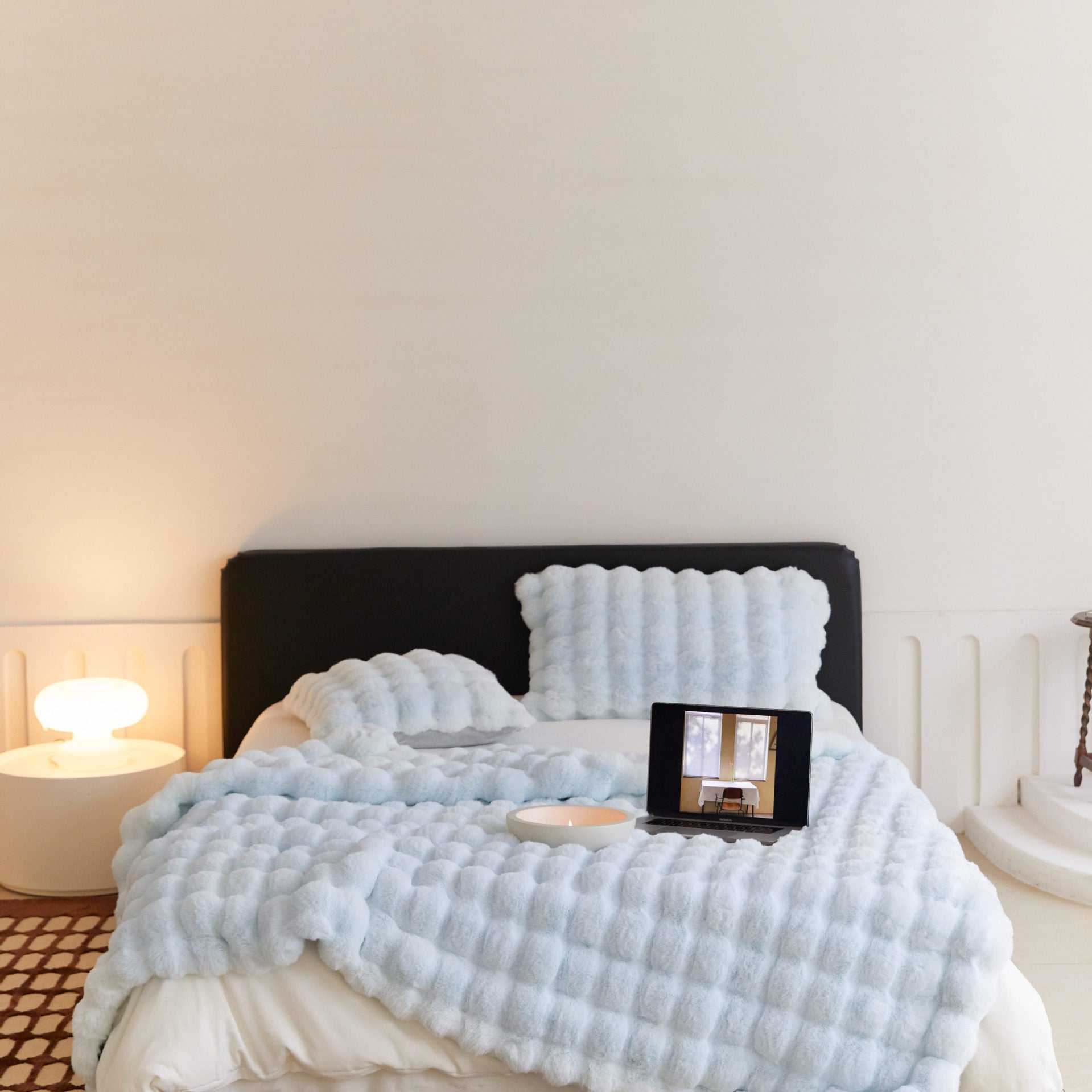 Bed with light blue textured blanket and pillows in a softly lit room.