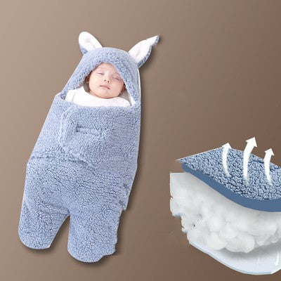 Baby wrapped in a blue fluffy swaddle with bunny ears on a brown background
