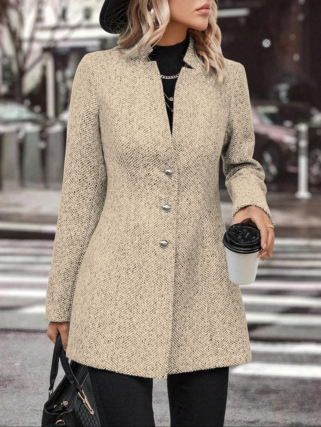 Woman in a beige coat crossing a street, holding a coffee cup.