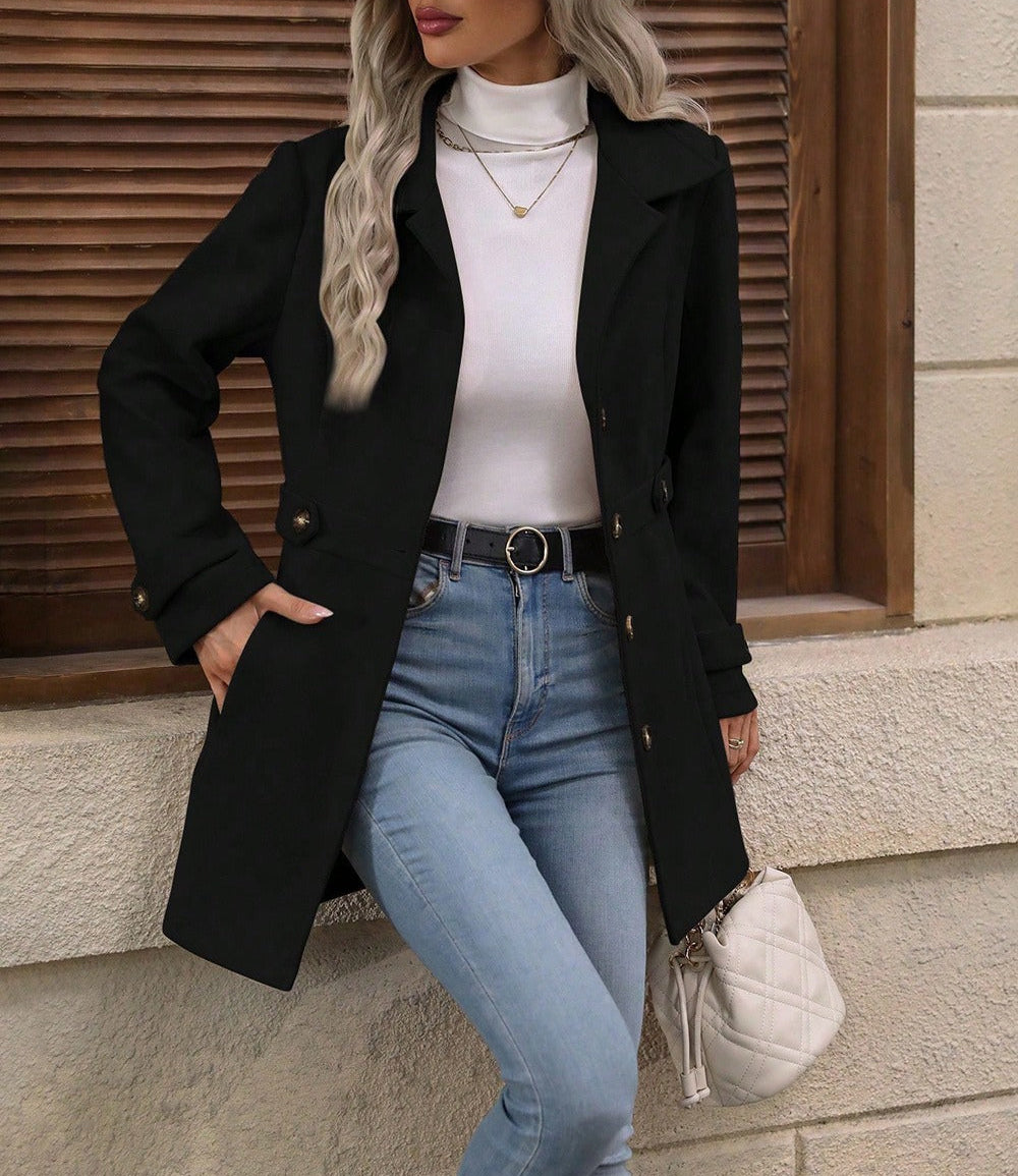 Woman wearing a black coat, white top, blue jeans, and beige hat against a wooden wall.