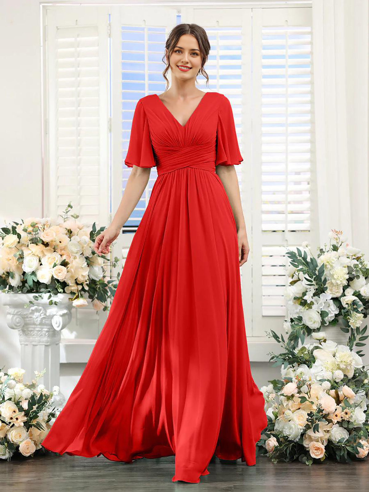 Woman in a red dress standing in front of floral decorations with white shutters in the background
