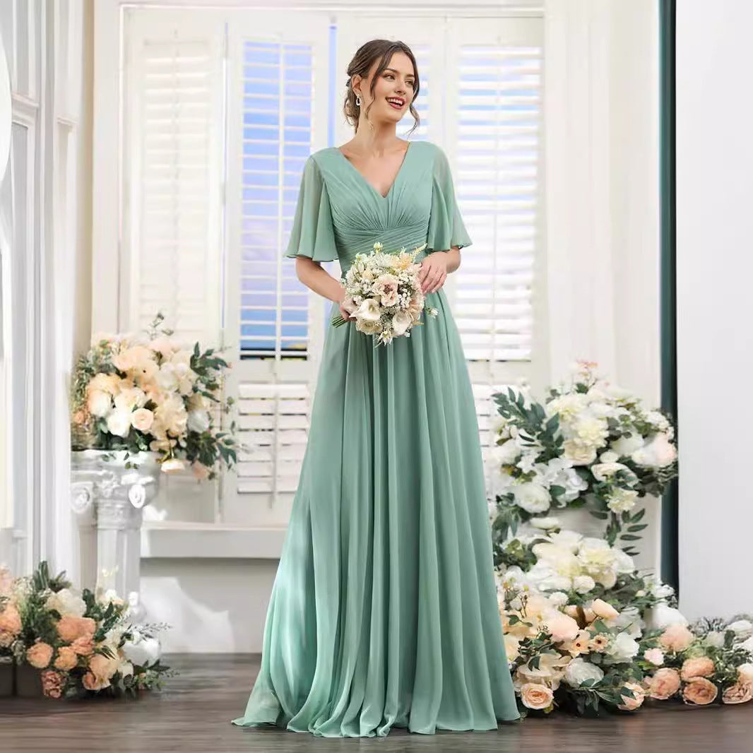 Woman in a mint green dress holding flowers in a decorated room with floral arrangements.