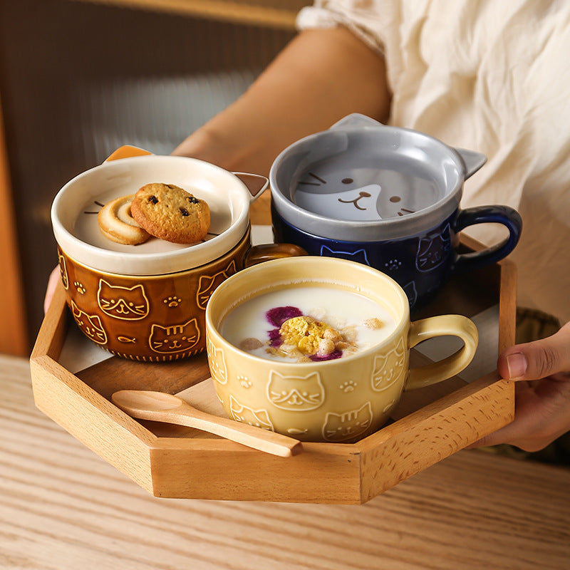 Three ceramic cups with cat designs on a wooden tray, containing food and drinks.