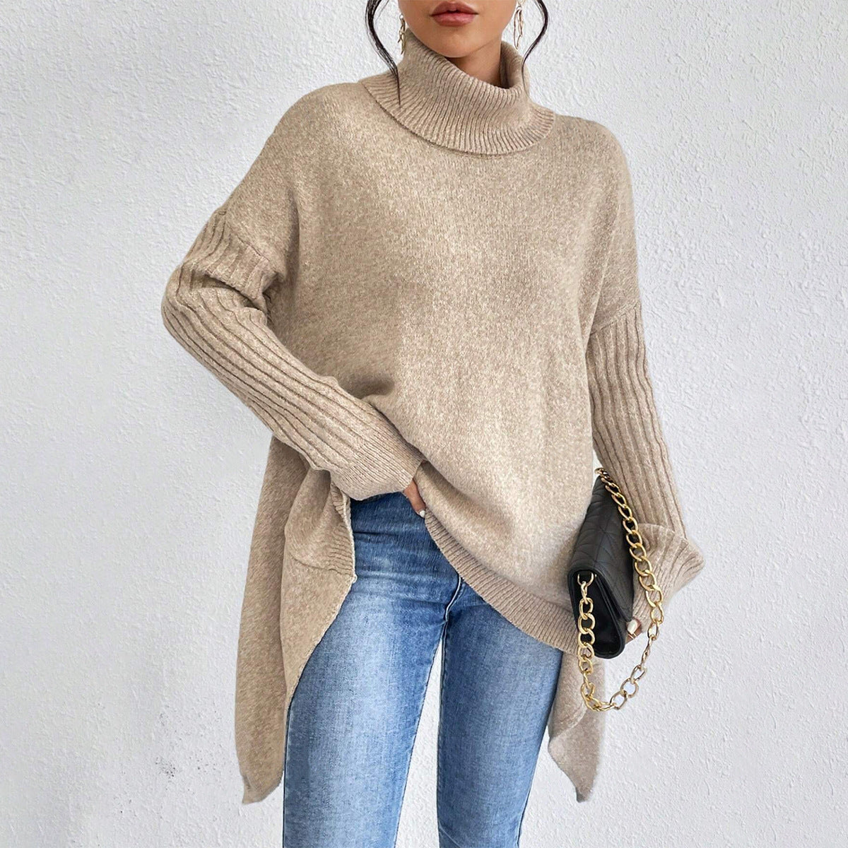 Person wearing a beige sweater and blue jeans against a white background