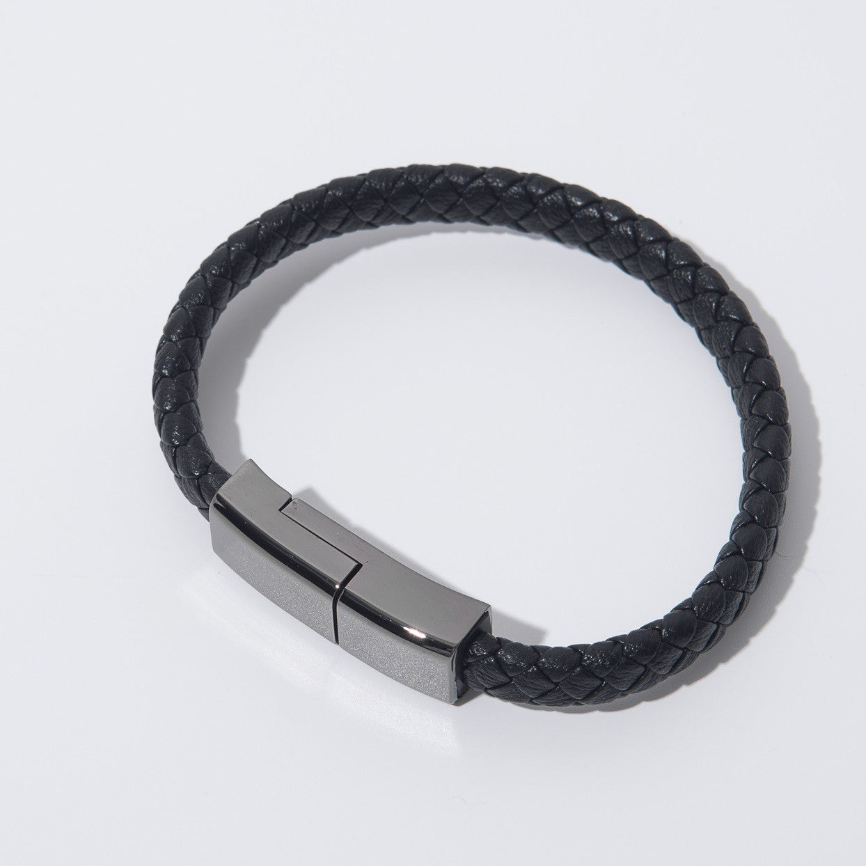 Black braided leather bracelet with a metallic clasp on a light gray background