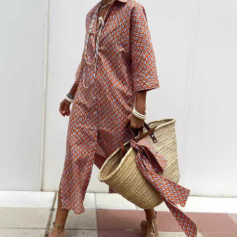 Person wearing a patterned dress holding a straw bag with a scarf, against a white wall.