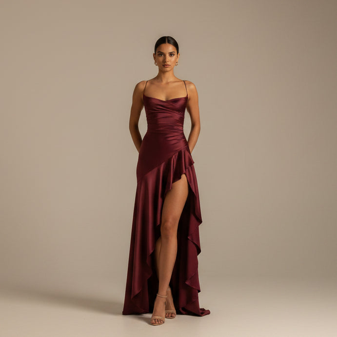 Woman wearing a burgundy evening gown with a high slit on a white background