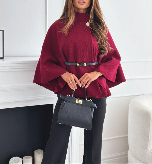 Woman wearing a burgundy poncho and black pants, holding a black handbag indoors.
