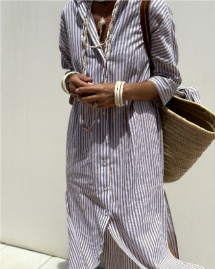 Person wearing a striped dress holding a woven bag against a light background