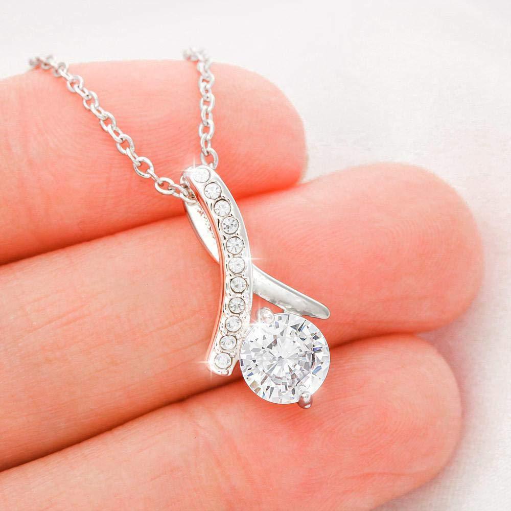 Silver necklace with a heart-shaped pendant held between fingers on a light background