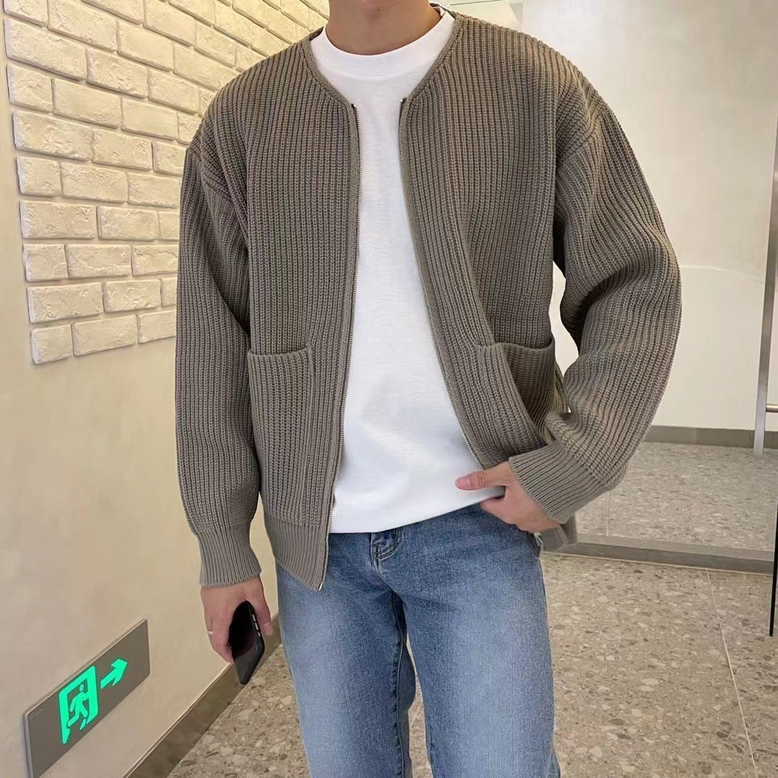 Person wearing a brown knitted cardigan, white shirt, and blue jeans in an indoor setting.