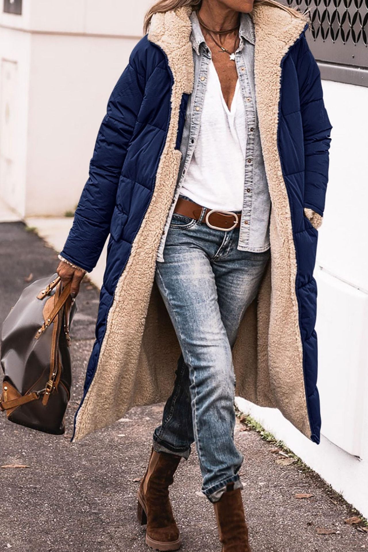 Person wearing a long blue coat with beige fur lining, jeans, and brown boots.