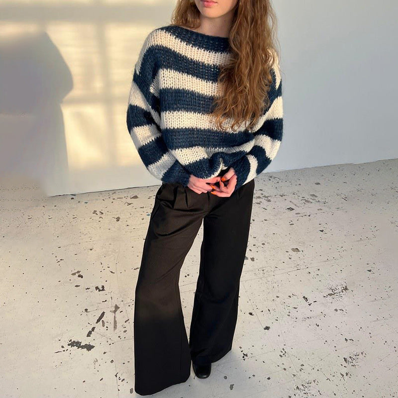 Person wearing a blue and white striped sweater and black pants in a minimal indoor setting.